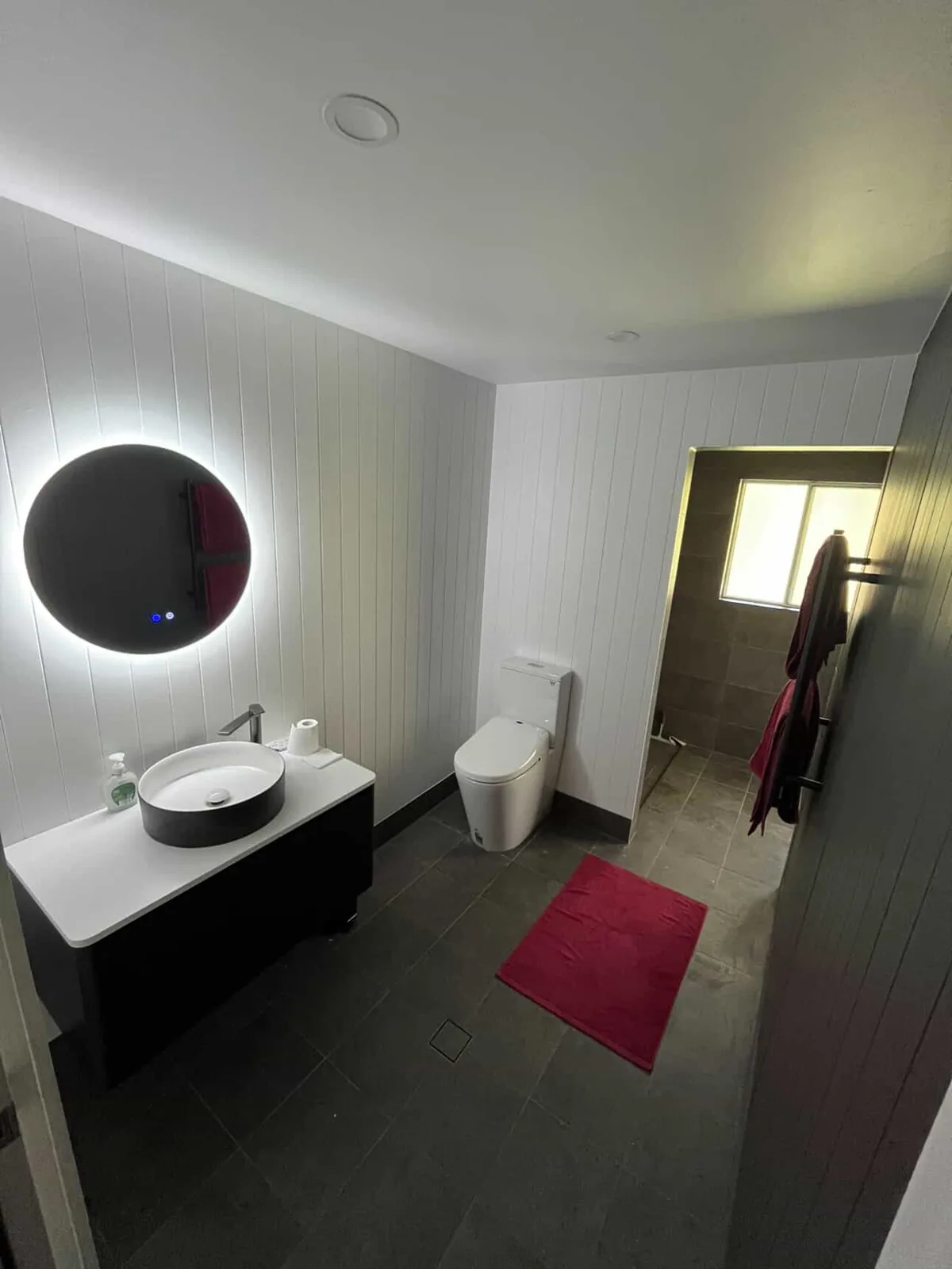 Round illuminated mirror, white vessel basin and dark wall-hung vanity