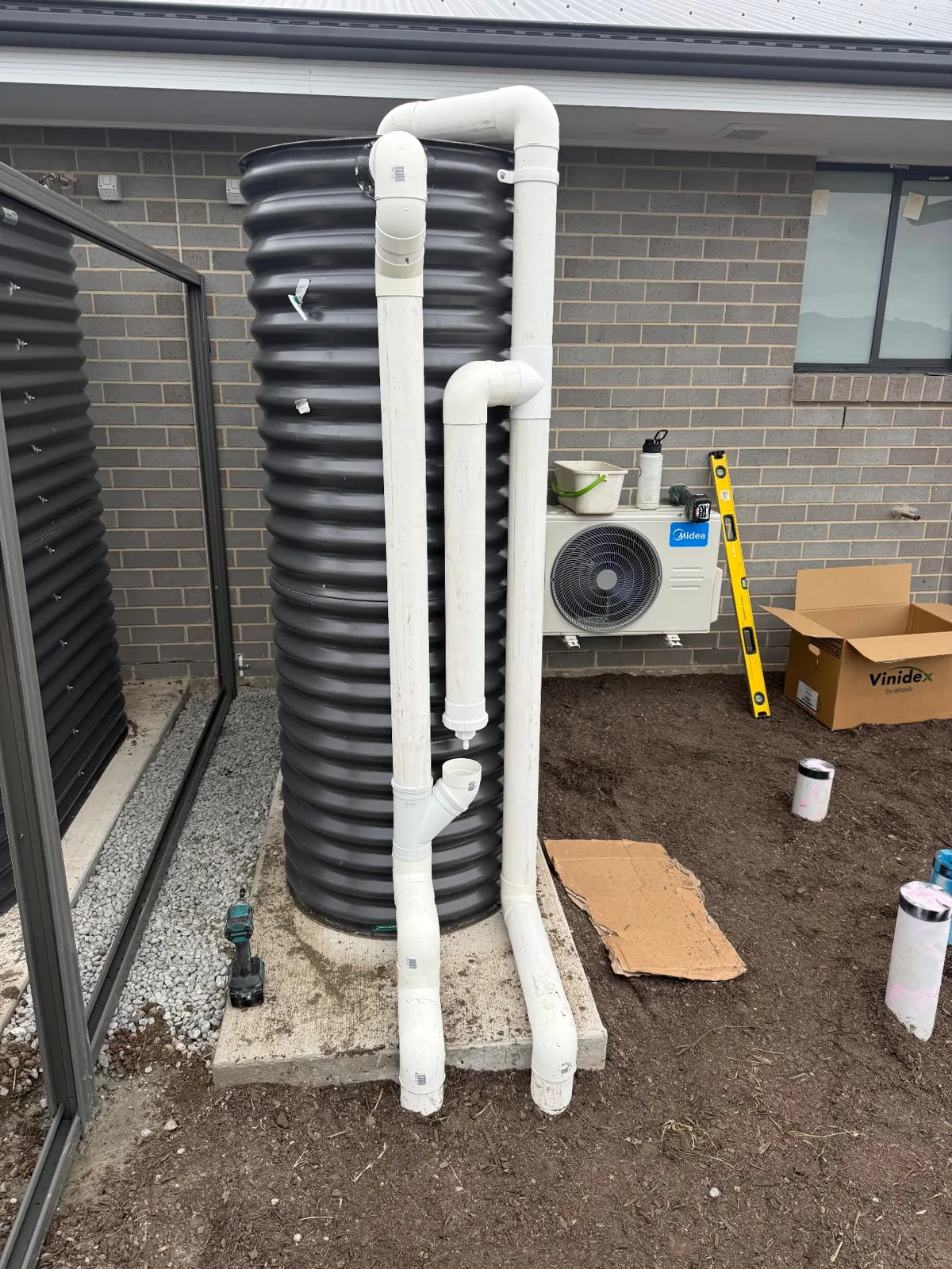 Black ribbed tank with white pipework beside a brick wall