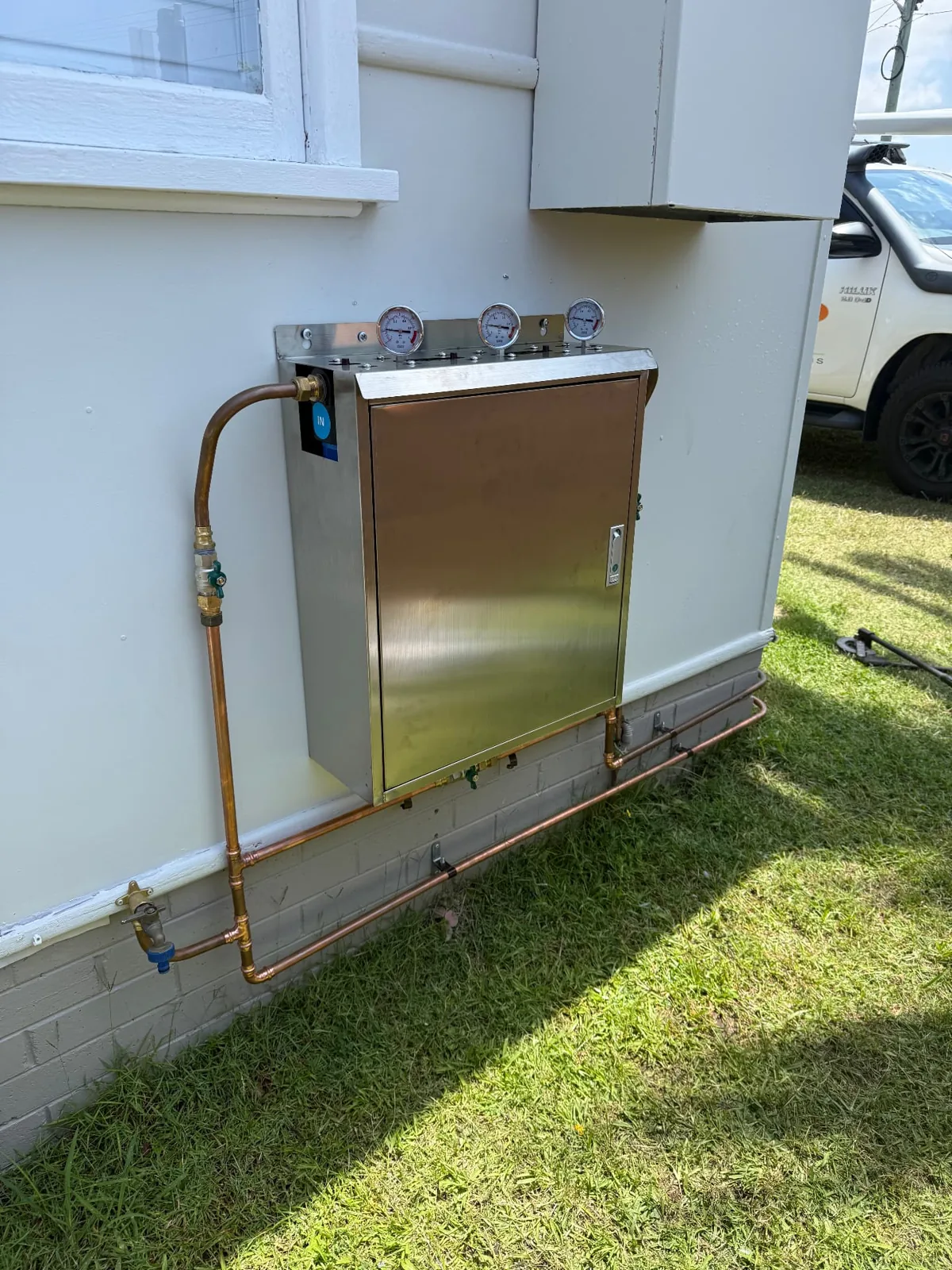 Metal cabinet with three pressure gauges and copper pipework on an exterior wall