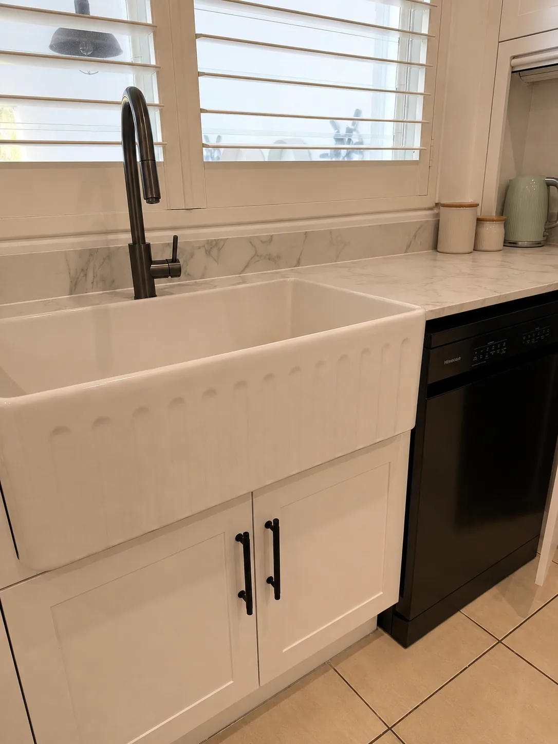 White kitchen sink with black mixer tap, white cabinetry and a black dishwasher
